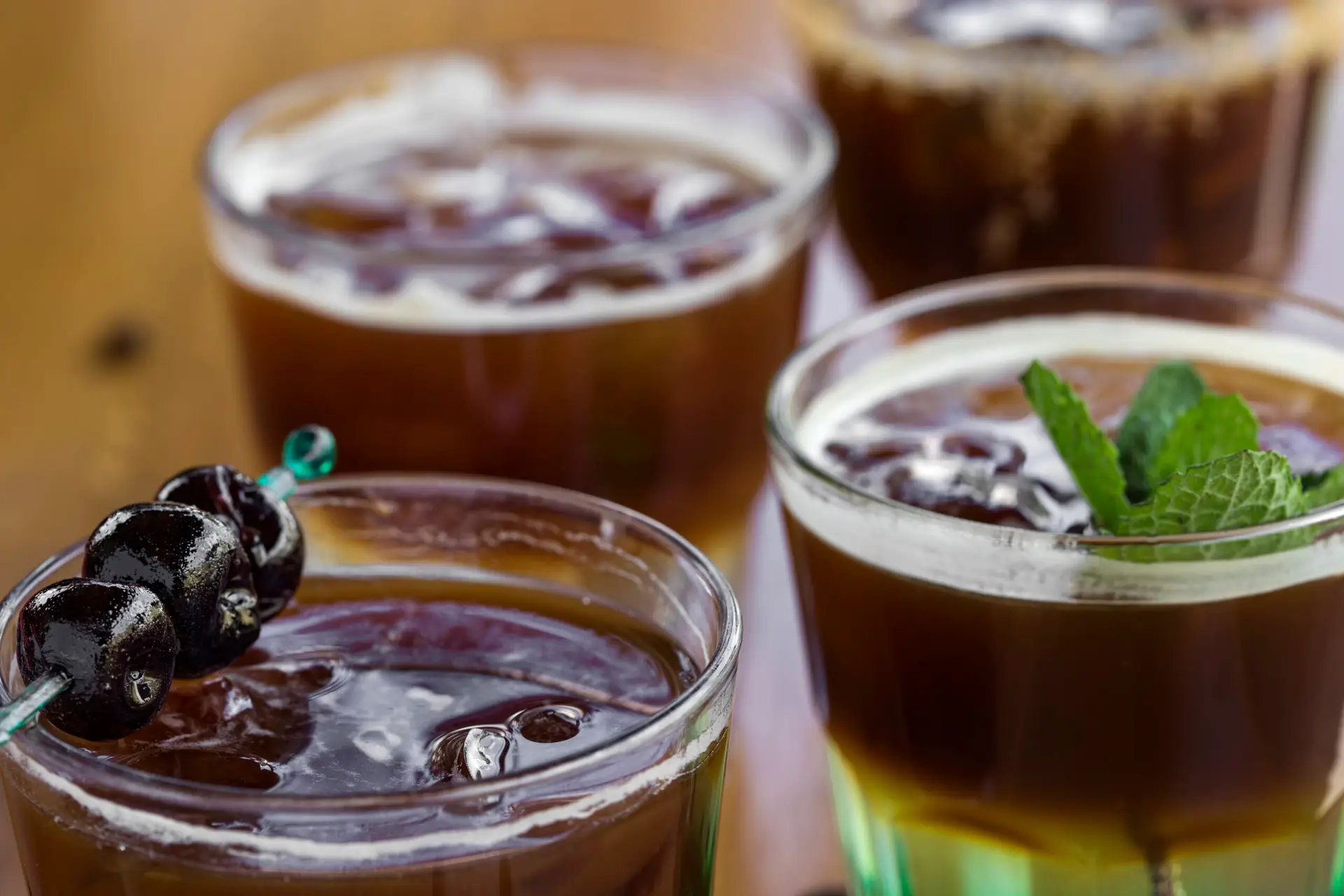 Cold coffees with mint leaves, orange, amarena fruits and ice cubes on the bar - close-up view